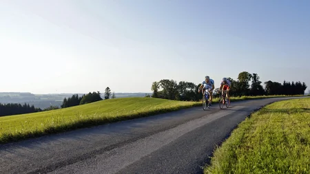 Ein Rennrad-Wochenende im SalzburgerLand – Salzkammergut © Rad WM Region Salzburg Eugendorf Zwei Rennradfahrer fahren auf Landstraße durch grüne hügelige Landschaft