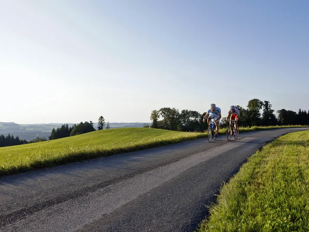 Ein Rennrad-Wochenende im SalzburgerLand – Salzkammergut © Rad WM Region Salzburg Eugendorf Zwei Rennradfahrer fahren auf Landstraße durch grüne hügelige Landschaft