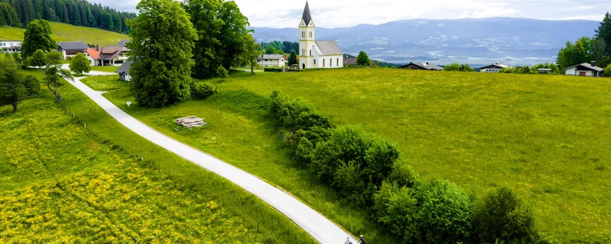 Two cyclists on path in green countryside near village with church