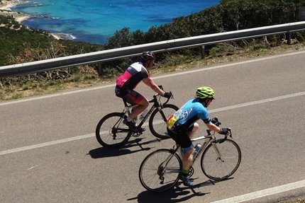 Two cyclists riding on coastal road overlooking the blue sea