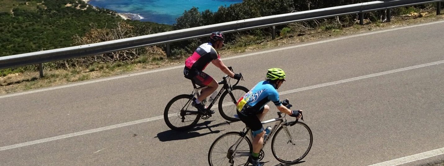 Two cyclists riding on coastal road overlooking the blue sea
