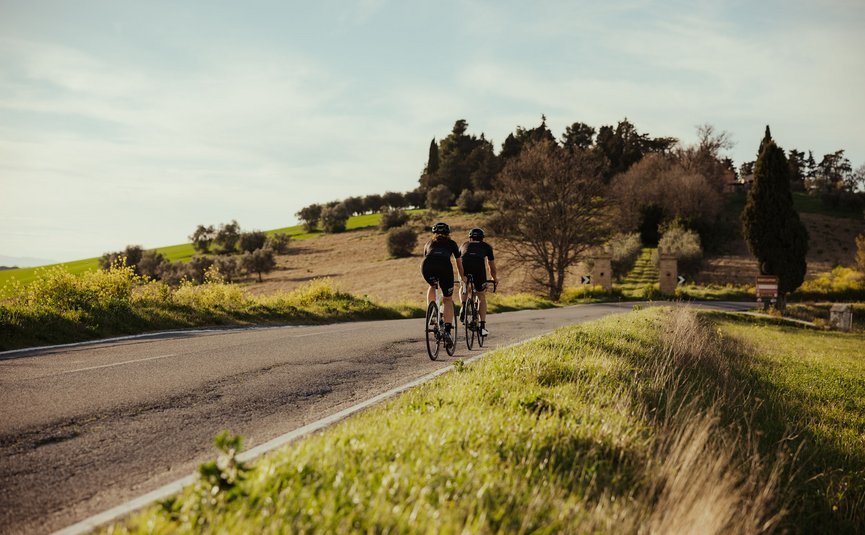 Due ciclisti su strada di campagna con campi verdi e alberi sullo sfondo