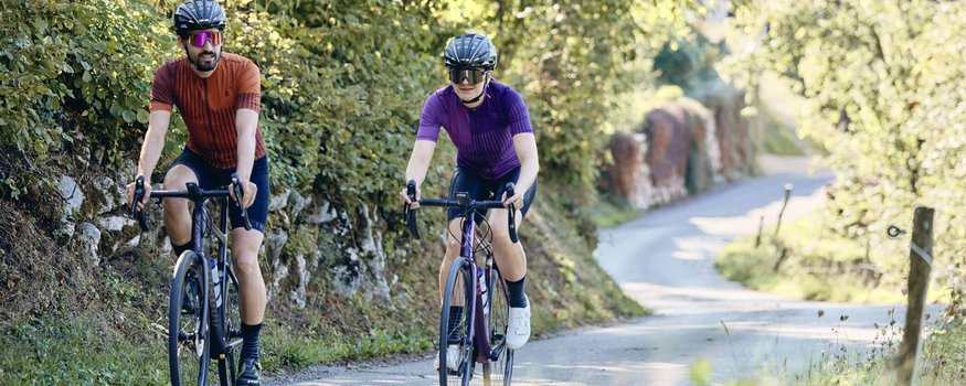 Twee fietsers op een landweg met groene begroeiing bij zonnig weer