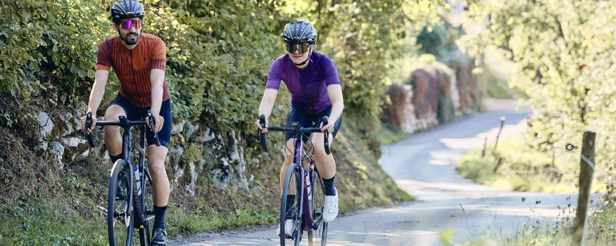 Zwei Radfahrer auf einer Landstraße mit grüner Vegetation bei Sonnenschein