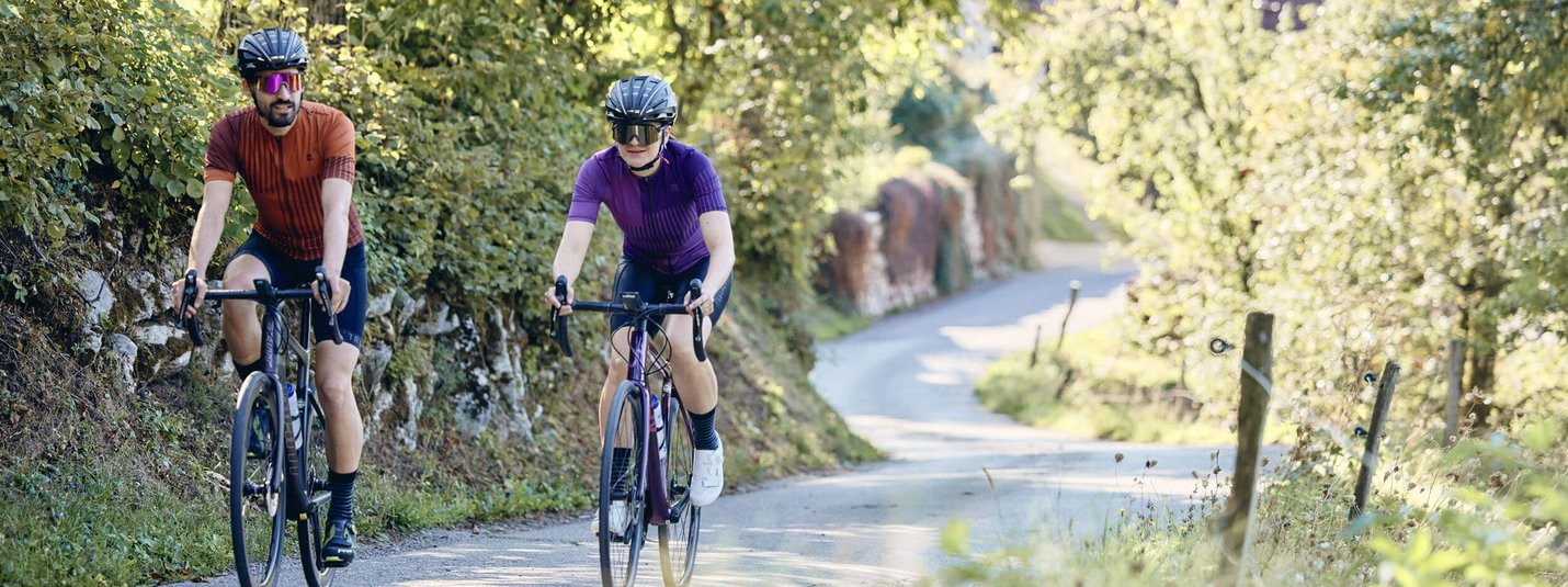Twee fietsers op een landweg met groene begroeiing bij zonnig weer