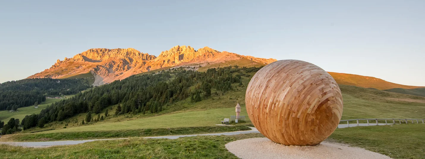 Reiter Joch © Günther Pichler - EyetotheDolomites Obereggen Holzskulptur in Form eines Eies auf einer Bergwiese bei Sonnenuntergang