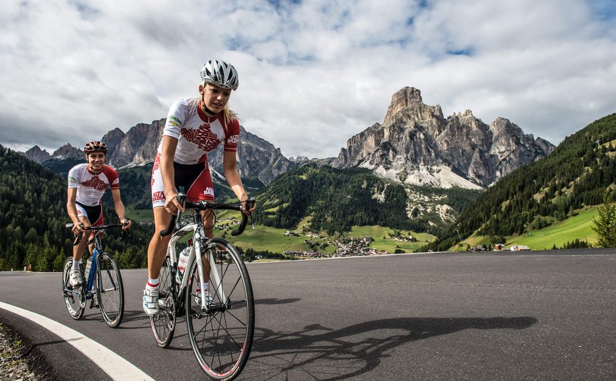 Two road cyclists riding on a mountain road under cloudy sky