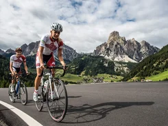 Two road cyclists riding on a mountain road under cloudy sky