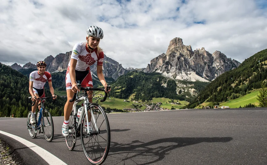 Vacanze in bici da corsa in Alta Badia © Paola Finali Due ciclisti su strada in montagna con cielo nuvoloso