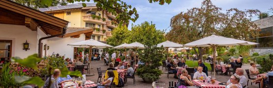 Camping Top weeks for campsite pros (2 persons) People sitting under umbrellas in garden restaurant with flowers and trees
