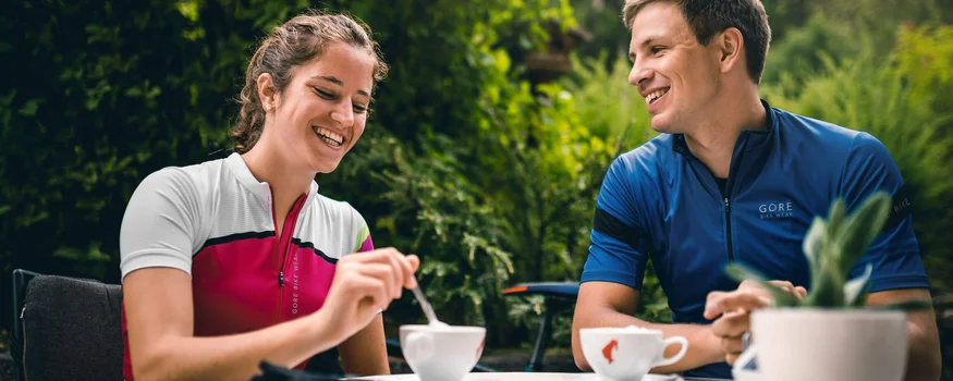 Warum Alta Badia auf jede Roadbike-Bucket-List gehört © Molography Zwei Radfahrer genießen Kaffee im Freien an einem Tisch