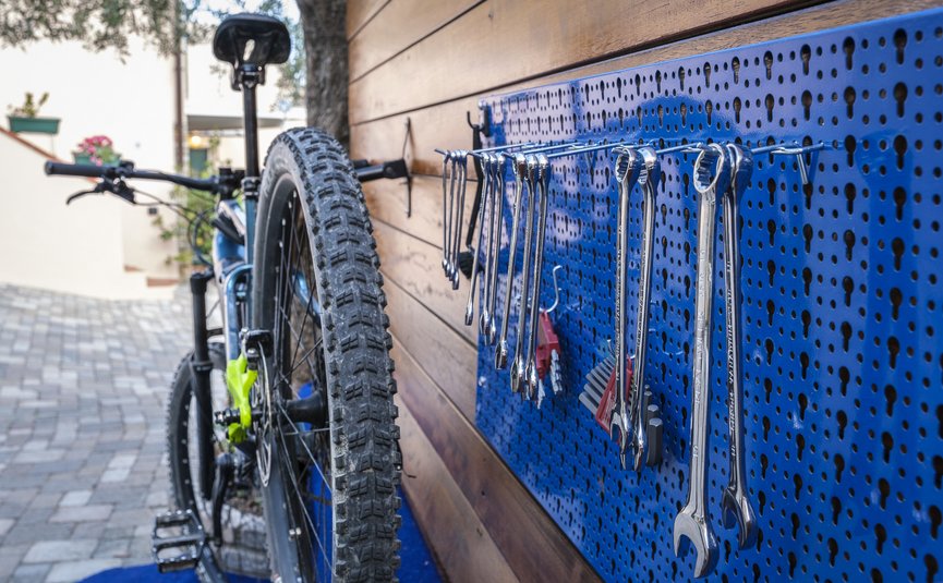 Bicicletta e attrezzi appesi a pannello porta attrezzi blu vicino a parete in legno