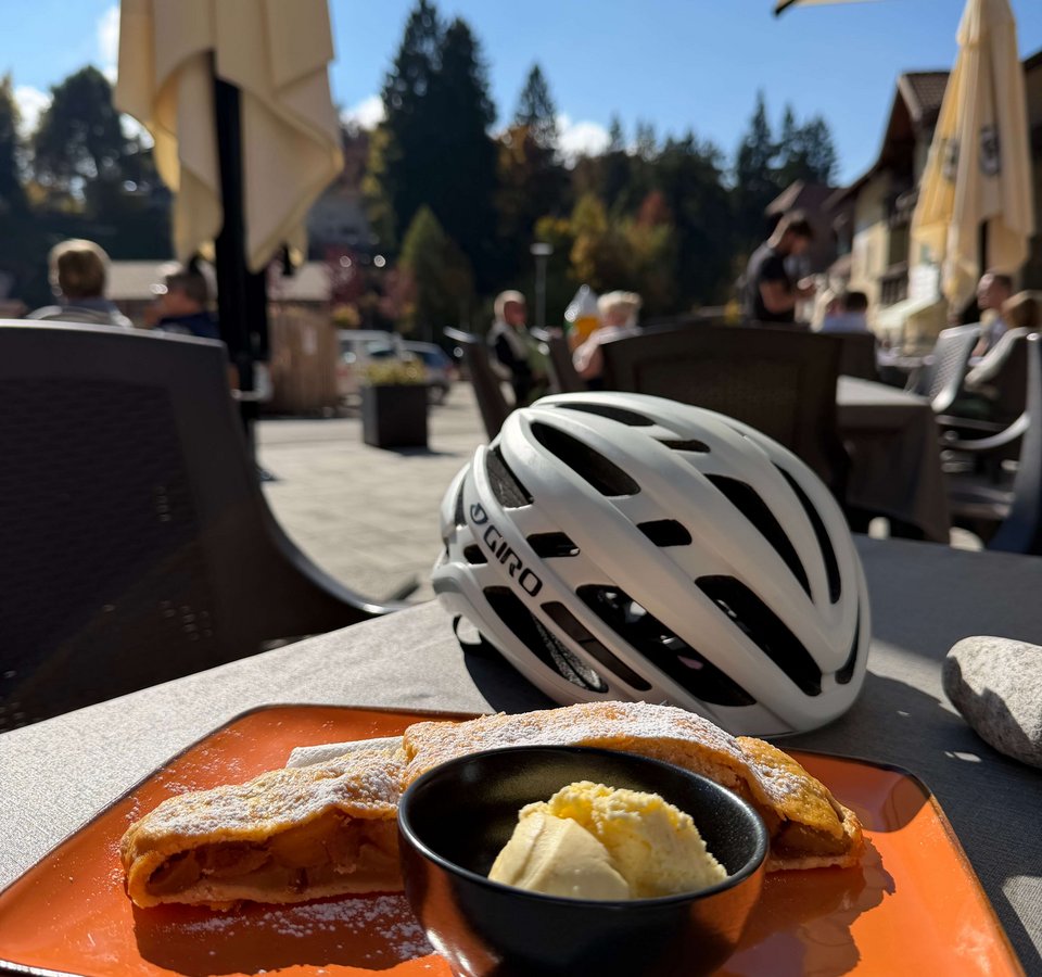 Apfelstrudel mit Vanilleeis auf orangefarbenem Teller neben Fahrradhelm im Außenbereich