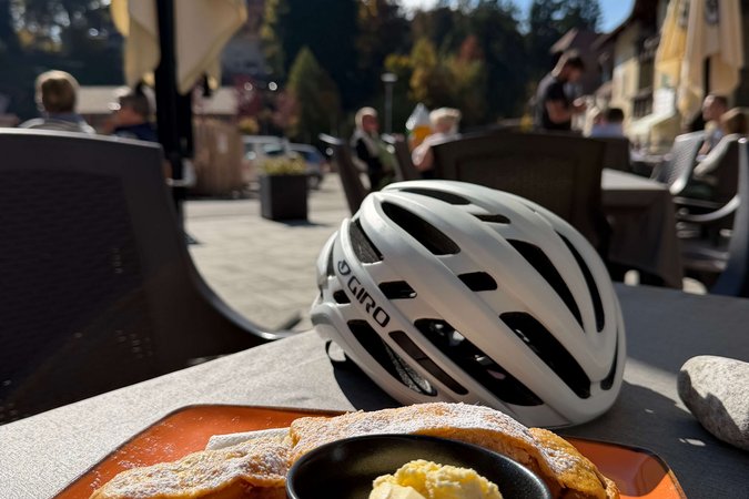 Apfelstrudel mit Vanilleeis auf orangefarbenem Teller neben Fahrradhelm im Außenbereich