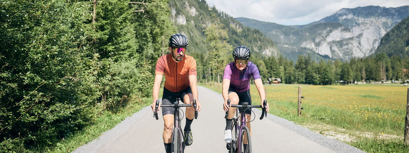 Loop Koper © Tobias Köhler Two cyclists riding on country road with forested mountains in sunny weather