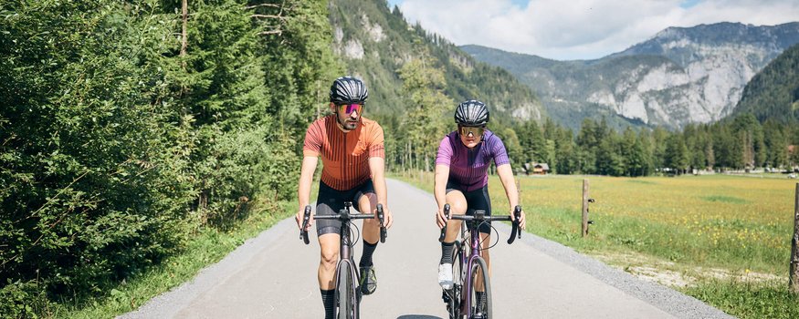 Rennradfahren im Land der Champions: Slowenien © Tobias Köhler Zwei Radfahrer auf Landstraße vor bewaldeten Bergen bei sonnigem Wetter