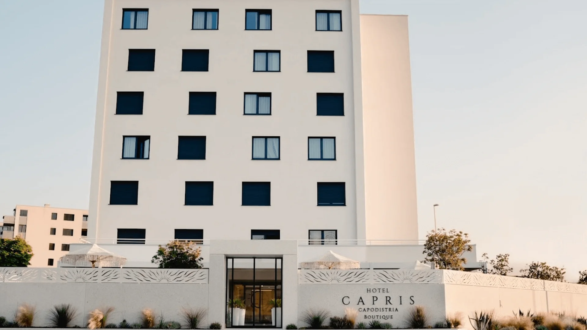Moderner weißer Hotelbau mit schwarzen Fensterläden und Namen vor der Fassade