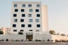 Collectief onderzoek © Hotel Capris Capodistria Boutique Modern wit hotelgebouw met zwarte luiken en naam op de gevel