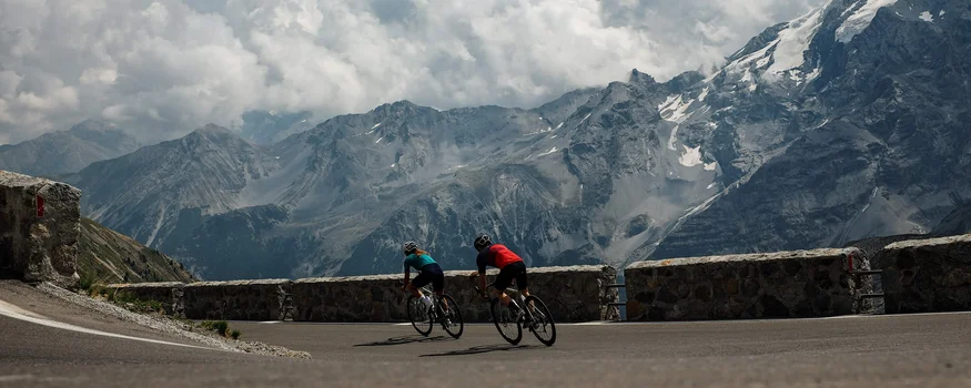 Zwei Radfahrer fahren auf bergiger Straße mit Nebel und Wolken