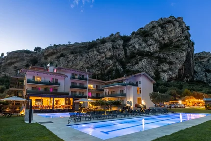 Hotel met verlicht zwembad voor een grote rots bij schemering
