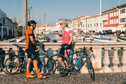 Twee fietsers praten op een brug over een kanaal met boten