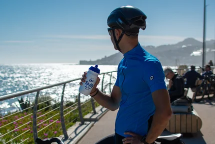Radfahrer macht Pause am Meer und hält eine Trinkflasche