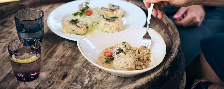 Zwischen Pass & Pasta in San Vigilio © Tobias Köhler Teller mit Knödeln und Pilzsoße auf einem Holztisch, jemand isst mit einer Gabel