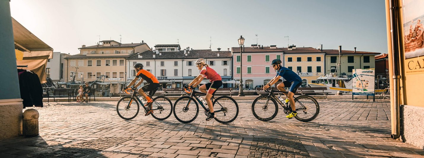 Tre ciclisti pedalano in una piazza soleggiata di una piccola città