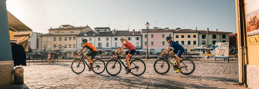 Three cyclists riding through a sunny square in a small town