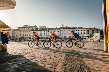 Three cyclists riding through a sunny square in a small town