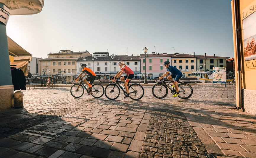 Three cyclists riding through a sunny square in a small town