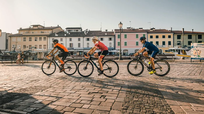 Adriatische Küste: Rennradurlaub mit Dolce Vita © Alex Moling Drei Radfahrer fahren durch einen sonnigen Platz in einer kleinen Stadt