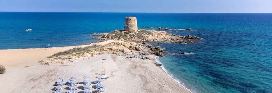 Spiaggia con ombrelloni blu e vecchia torre di pietra su isolotto roccioso
