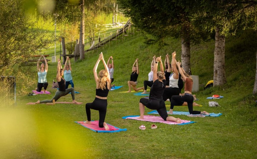 Gruppo che pratica yoga all'aperto su prato verde con alberi