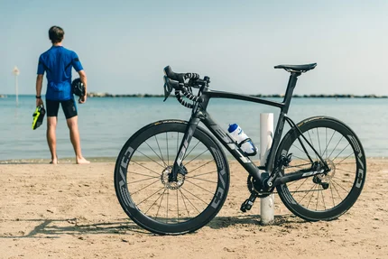 Black road bike on beach with cyclist looking at the sea