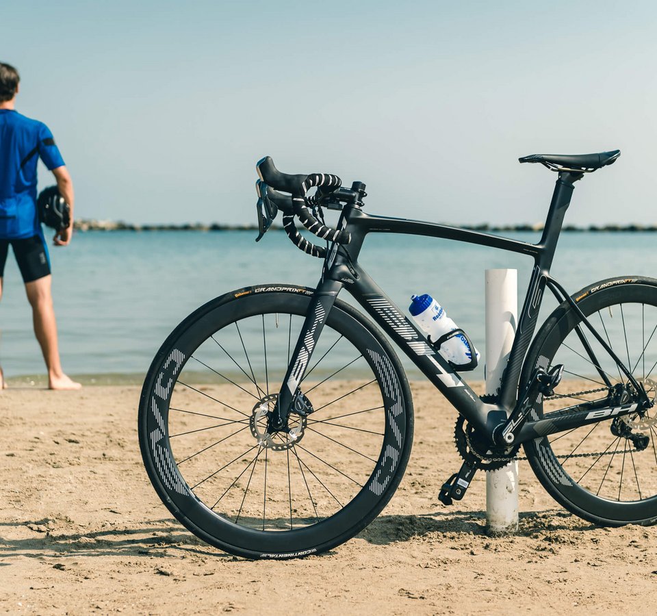 Schwarzes Rennrad am Strand, Radfahrer blickt aufs Meer