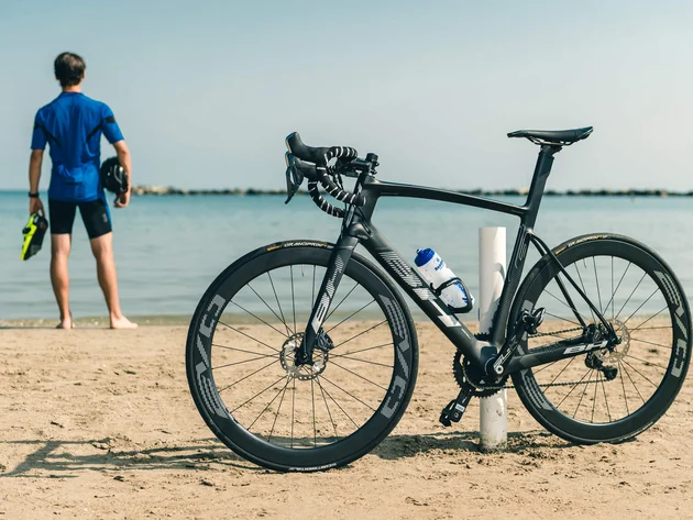 Bici da corsa nera sulla spiaggia, ciclista guarda il mare