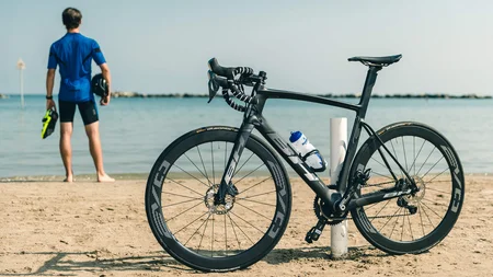 Bici da corsa nera sulla spiaggia, ciclista guarda il mare
