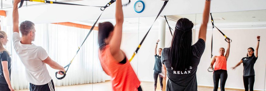Gruppe von Menschen beim TRX-Training in einem Fitnessstudio mit Spiegel