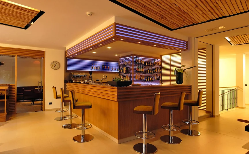 Area bar moderna con bancone in legno e sgabelli con luce calda