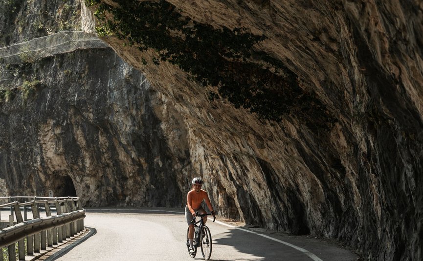 Radfahrer auf kurviger Straße unter Felsen mit Schatten