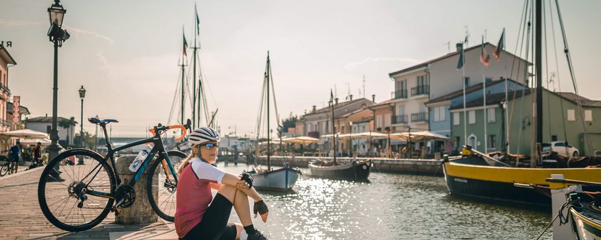 Radfahrerin sitzt am Hafen mit Booten und Fahrrad im Sonnenschein