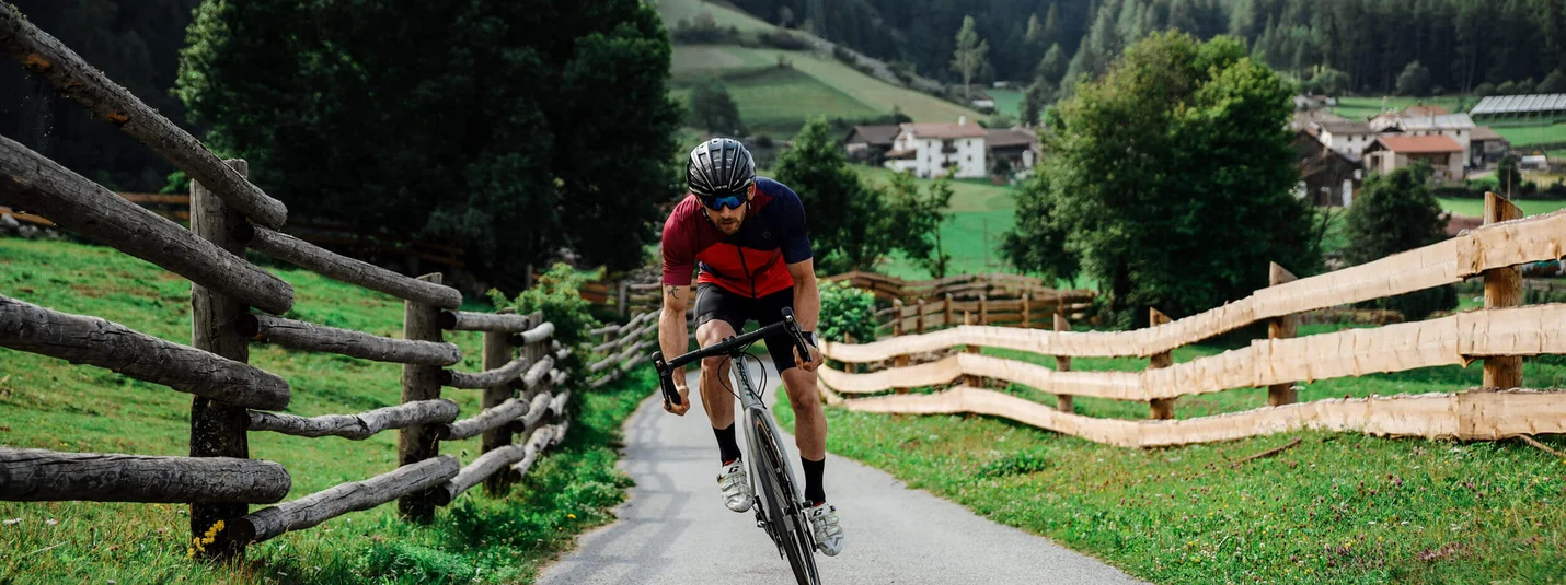 Passo Flüela © Felix Saller Uomo in bici da corsa su strada di campagna con recinzioni in legno e montagne