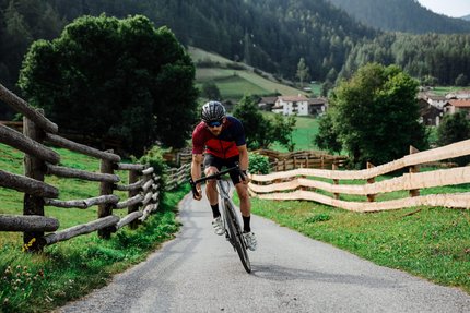 Uomo in bici da corsa su strada di campagna con recinzioni in legno e montagne