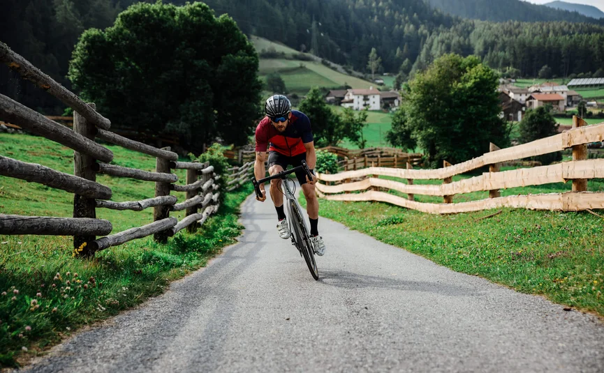 Man cycling on rural road with wooden fences and mountains in background