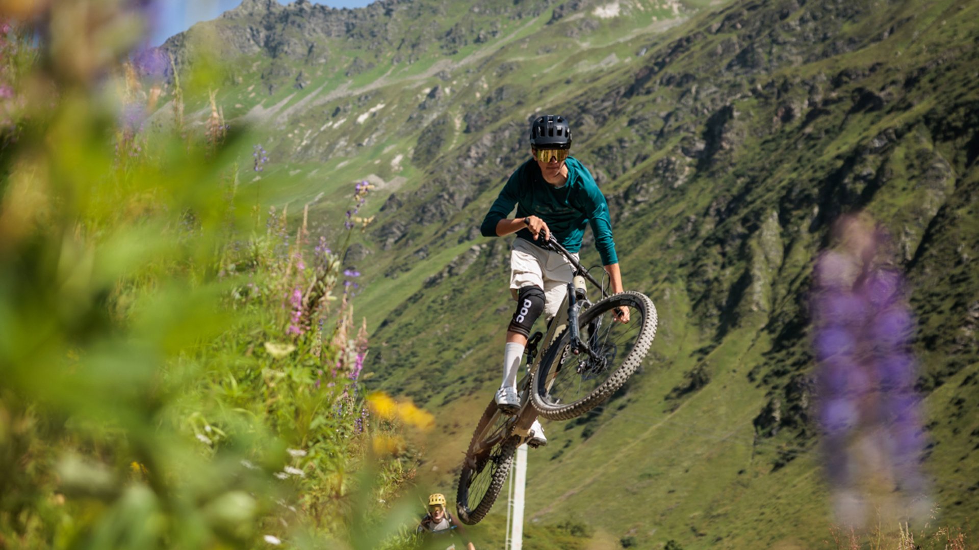 Mountainbiker springt auf Bergpfad mit grünen Hügeln im Hintergrund