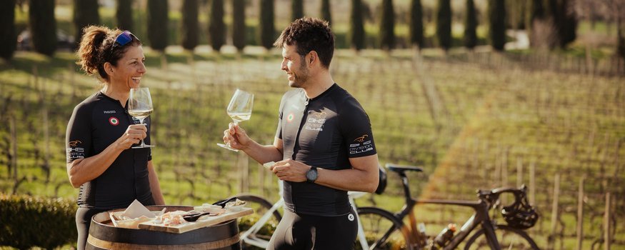 Zwei Radfahrer genießen Wein und Snacks an einem Weinfass im Weinberg