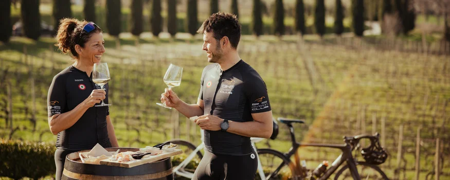 Zwei Radfahrer genießen Wein und Snacks an einem Weinfass im Weinberg