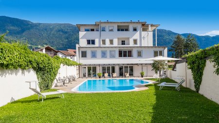 Weißes Hotel mit Außenpool, Liegestühlen und Bergblick bei klarem Himmel