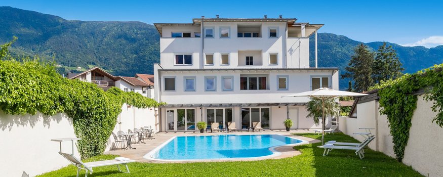 Weißes Hotel mit Außenpool, Liegestühlen und Bergblick bei klarem Himmel